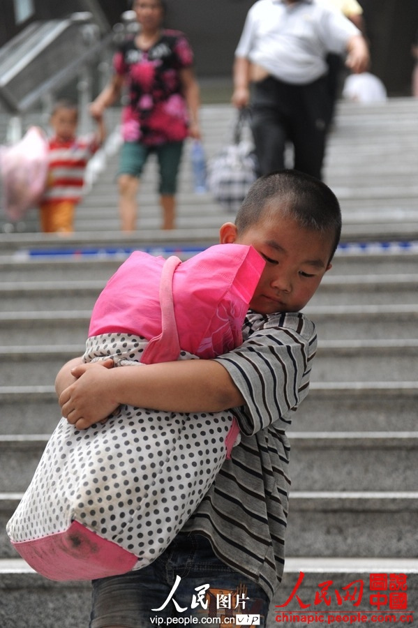 A child accompanied by adult takes the train to spend holidays with his parents working in city at Fuyang Railway Station, east China's Anhui province, July 1, 2013. (photo/vip.people.com.cn)