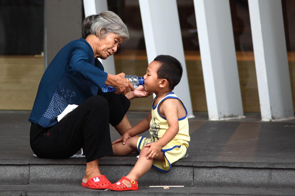 An old woman helps a child drink beverage in the heat, Shanghai, July 4, 2013. On that day, the highest temperature hit 38 Celsius degrees in Shanghai and the city’s meteorological agency issued the second orange high temperature this summer. (Xinhua/Yang Shichao)