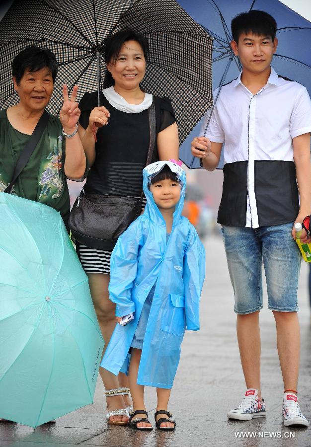 People pose for pictures in rain at the Tiananmen Square in Beijing, capital of China, July 9, 2013. Many tourists continue to come to enjoy the scenery of the capital city while Beijing witnessed frequent rainfall recently. The local meteorological observatory issued a warning on torrential rains from Tuesday to Wednesday in Beijing. (Xinhua/Chen Yehua)