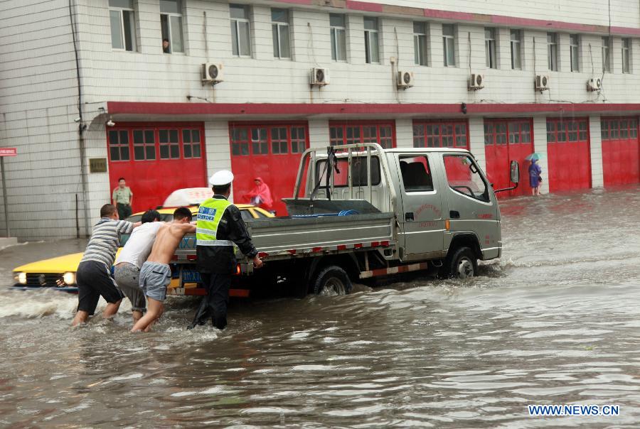 A policeman and citizens push a vehicle on a flooded road in rainstorm-hit Binzhou City, east China's Shandong Province, July 10, 2013. (Xinhua/Liu Chunying)