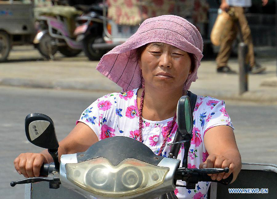 A woman rides on a road as heat wave hits Shangqiu City, central China's Henan Province, July 10, 2013. The highest temperature reached 37 degrees Celsius in the city on Wednesday. (Xinhua/Wang Song)