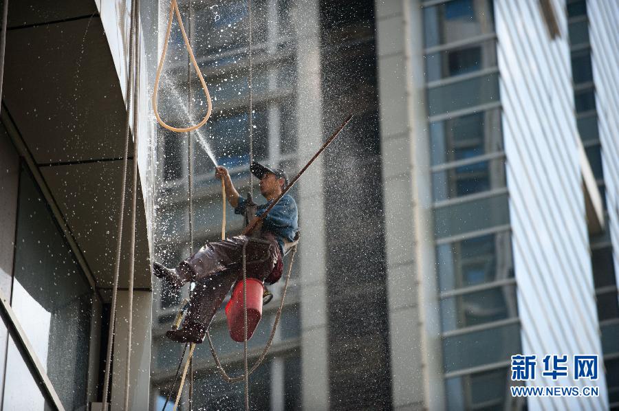 A "Spider-man" braves the heat and cleans the windows of a high-rising building in Guangzhou, capital of south China's Guangdong province on June 27, 2013. Cleansers of surface of high-rise building are also called "spider-men". (Photo/Xinhua) 