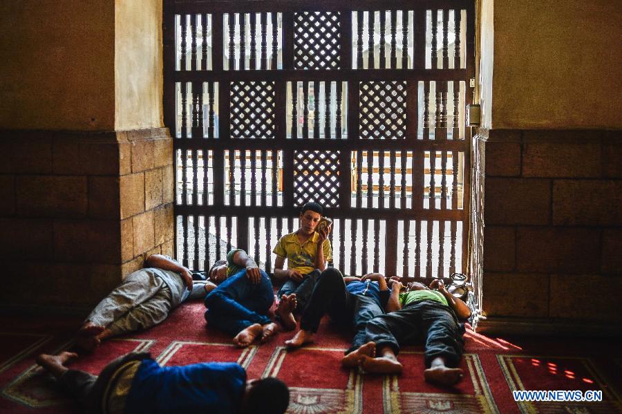 An Egyptian young man reads Quran while others sleep waiting for the time to break their fast at Al-Azhar Mosque on the first day of the holy month of Ramadan in Cairo, Egypt, July 10, 2013. (Xinhua/Qin Haishi)