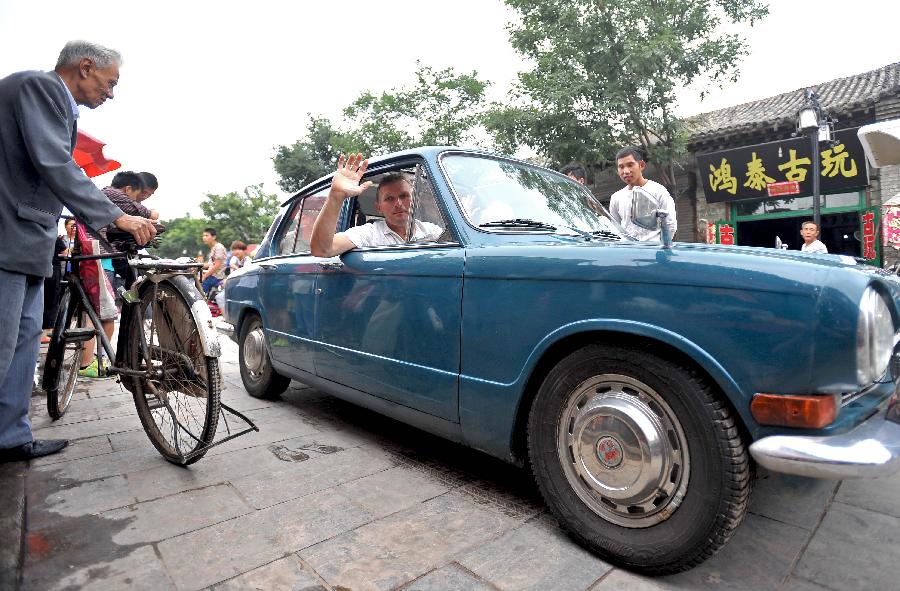 British Clive Raven waves to local residents while driving a Triumph 1300 made in 1967, in Pingyao, north China's Shanxi Province, July 10, 2013. [Photo: Xinhua] 