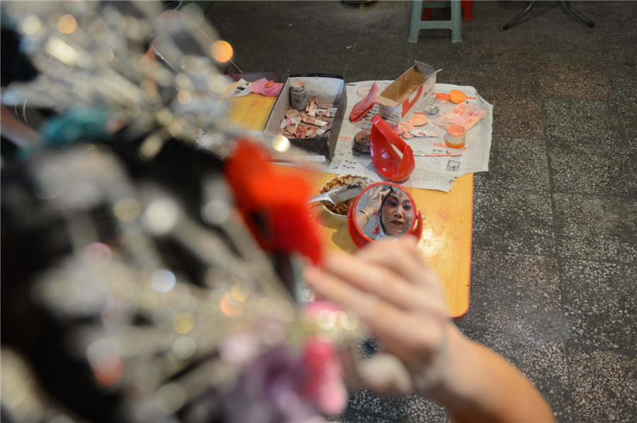 A member of the Haha Tune troupe puts on make-up in Kouzhuang village, Mumendian town, Qing county, Hebei province, July 10, 2013. (Xinhua)