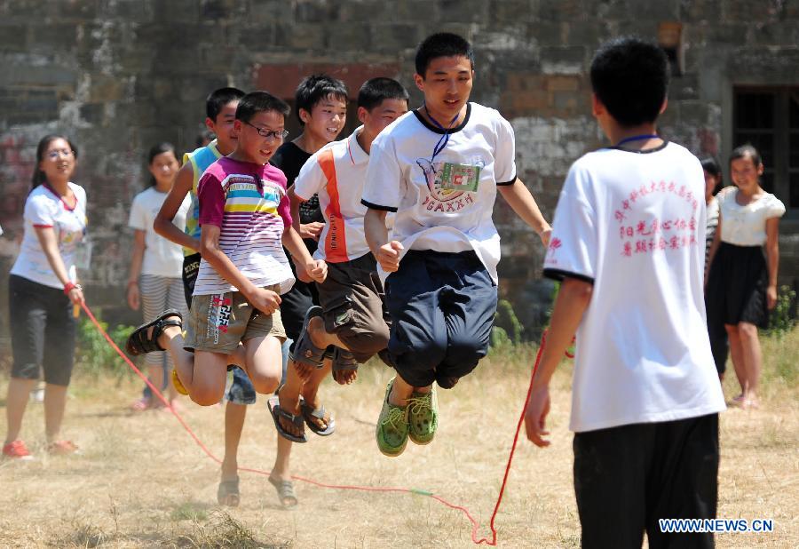 Volunteers play rope skipping with left-behind children at Maolong Primary School of Wangdun Township in Duchang County, east China's Jiangxi Province, July 11, 2013. Twenty-four student volunteers of the Wuchang Branch of Huazhong University of Science and Technology came to the primary school to carry out 20-day education support activities for about 200 left-behind children in the summer vacation. (Xinhua/Hu Guolin)