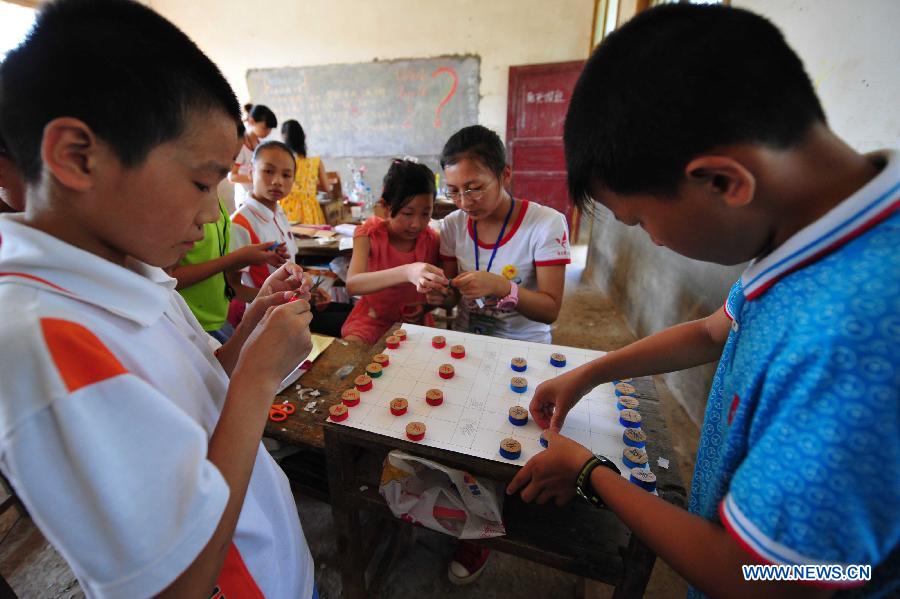Volunteers teach left-behind children to make chess pieces with cartons at Maolong Primary School of Wangdun Township in Duchang County, east China's Jiangxi Province, July 11, 2013. Twenty-four student volunteers of the Wuchang Branch of Huazhong University of Science and Technology came to the primary school to carry out 20-day education support activities for about 200 left-behind children in the summer vacation. (Xinhua/Hu Guolin)