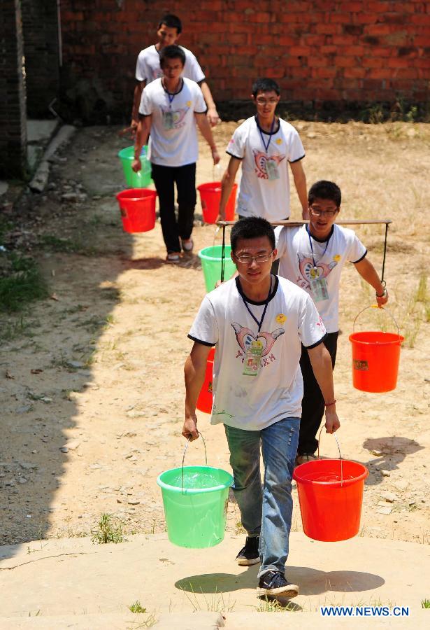 Volunteers carry water for cooking at Maolong Primary School of Wangdun Township in Duchang County, east China's Jiangxi Province, July 11, 2013. Twenty-four student volunteers of the Wuchang Branch of Huazhong University of Science and Technology came to the primary school to carry out 20-day education support activities for about 200 left-behind children in the summer vacation. (Xinhua/Hu Guolin) 