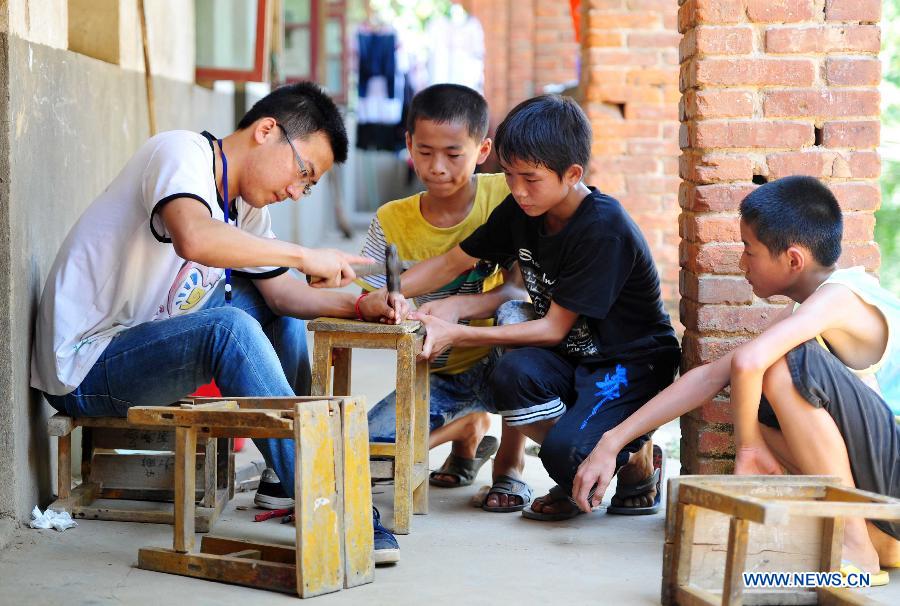 A volunteer mends a chair for left-behind children at Maolong Primary School of Wangdun Township in Duchang County, east China's Jiangxi Province, July 11, 2013. Twenty-four student volunteers of the Wuchang Branch of Huazhong University of Science and Technology came to the primary school to carry out 20-day education support activities for about 200 left-behind children in the summer vacation. (Xinhua/Hu Guolin)