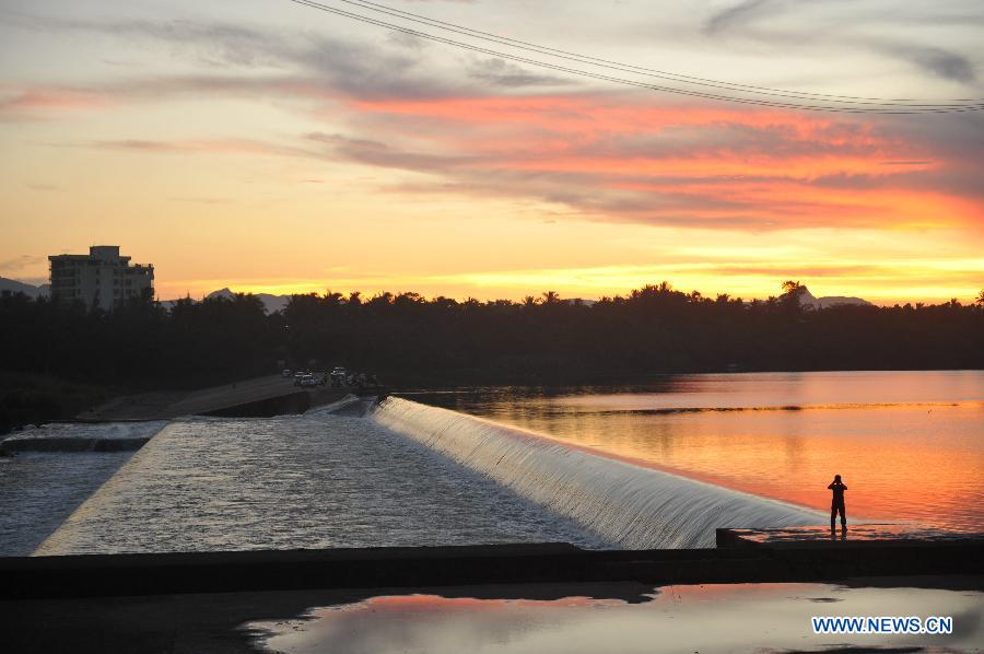 A local resident takes photos of the sunset by the Wanquan River in Qionghai City, south China's Hainan Province, July 11, 2013. (Xinhua/Meng Zhongde)