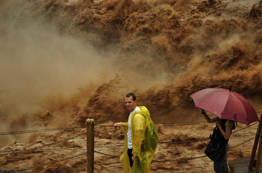 A tourist poses for a photo with the Hukou Waterfall of the Yellow River from the site in Jixian County, north China's Shanxi Province, July 12, 2013. Triggered by non-stop heavy rainfall in the upper reaches, the rising water level of the Yellow River surged the Hukou Waterfall, attracting many visitors. (Xinhua/Lu Guiming) 