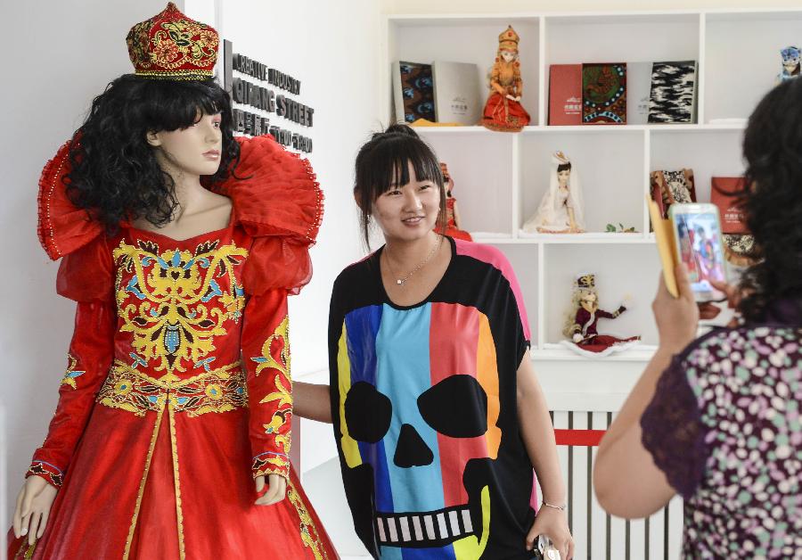 A visitor poses for photos with a displayed ethnic costume in an exhibition held in Urumqi, capital of northwest China's Xinjiang Uygur Autonomous Region, July 12, 2013. The first session of Xinjiang Presents Design Competition that kicked off from April has received more than 900 pieces of artworks including sculptures, paintings, embroidery, paper cutting and pottery. (Xinhua/Wang Fei)  