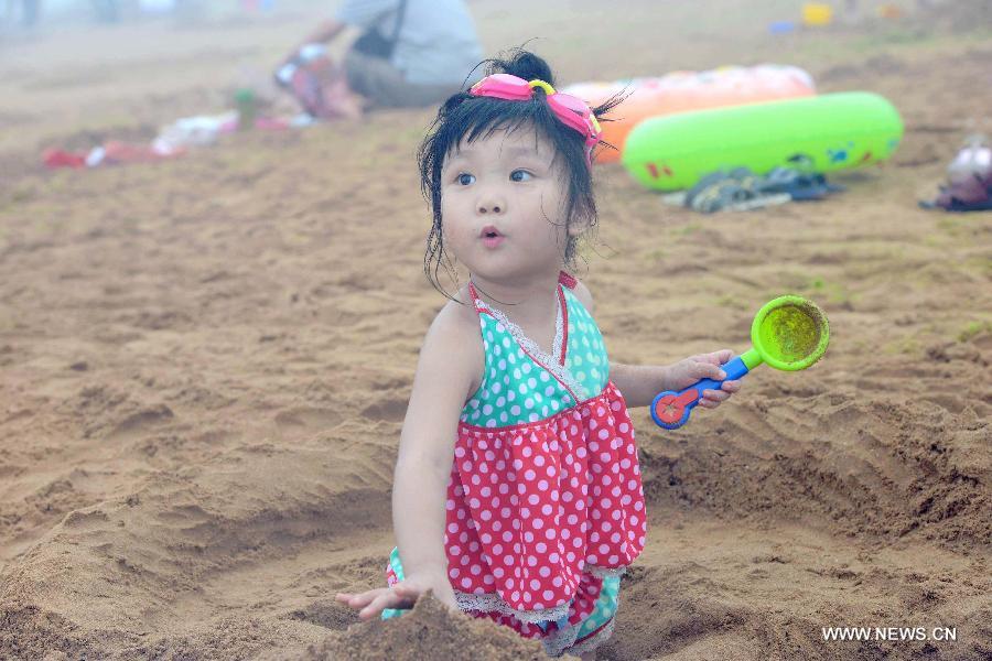 A little girl plays on the Jinshatan bathing beach in Qingdao, east China's Shandong Province, July 13, 2013. Saturday marks the beginning of the hottest part of summer. Many people came to the seashore to spend a cool weekend. (Xinhua/Yu Fangping)