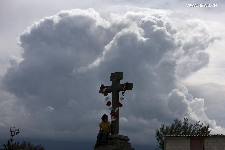 Photo taken on July 13, 2013 shows a boy seats by a cross while a cloud of ashes rises from the Popocatepetl volcano in San Nicolas de los Ranchos, Puebla, central Mexico. (Xinhua/Guillermo Arias) 