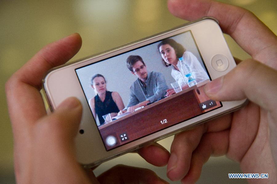 A media worker views a photo by cellphone that shows Former U.S. spy agency contractor Edward Snowden (C) attending a meeting with Russian human rights activists and lawyers at Moscow's Sheremetyevo International Airport, Russia, on July 12, 2013. Edward Snowden plans to apply for political asylum in Russia, a Russian parliamentarian said Friday after meeting with the stranded whistleblower. (Xinhua/Jiang Kehong)