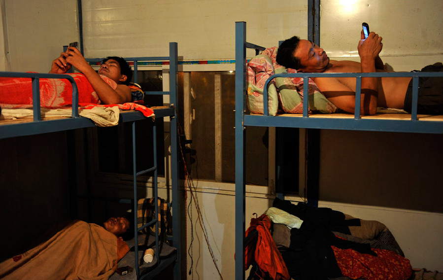 Migrant workers send text messages instead of calling their wives to save money after a day’s work, lying on their bed in the shabby temporary dormitory. They rarely shared their homesickness with each other for fear that other co-workers would look down on them. (Photo/ Guangming Online) 
