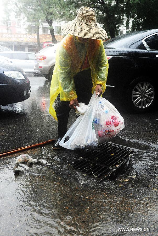 A cleaner cleans rubbish near a manhole on a road in the rain in Beijing, capital of China, July 15, 2013. Beijing's meteorologic center on Monday issued a yellow alert for rainstorm, as the lasting rainfall affected Beijing's traffic. (Xinhua/He Junchang) 