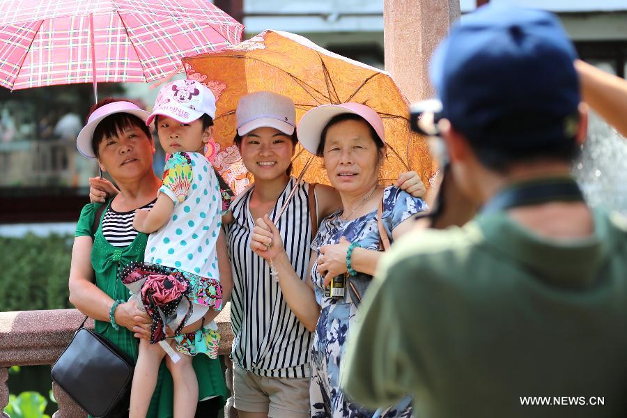 Tourists pose for photo with umbrellas to shade themselves from the sun in Shanghai, east China's municipality, July 15, 2013. Local meteorological observatory issued an yellow-coded alert of heat at noon on July 15, 2013. (Xinhua/Yang Shichao)  