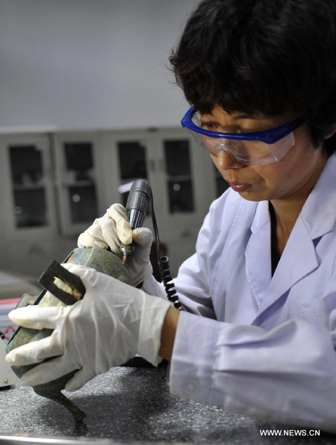 Liu Jiping, an expert on cultural relics preservation, repairs a bronze "Ding", a type of ancient Chinese vessel, at the relics conservation center of the museum of Tianshui City, northwest China's Gansu Province, July 15, 2013. A total of six cultural relics preservation experts of the museum conduct the conservation work on relic items here. They use modern technology as well as traditional handicraft to repair and restore cultural relic fragments and damaged bronze wares. (Xinhua/Chen Bin)