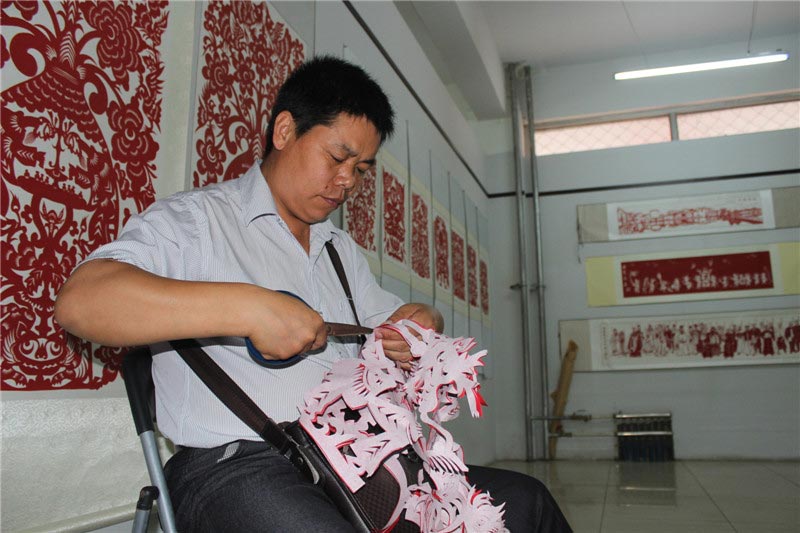A folk artist from Anhui province creates a paper-cut design at the 4th Chinese paper-cut art festival in Wei county, Hebei province. The festival was held July 8-10 and featured works from over 360 folk artists around China. (China Daily/Zhou Panpan)