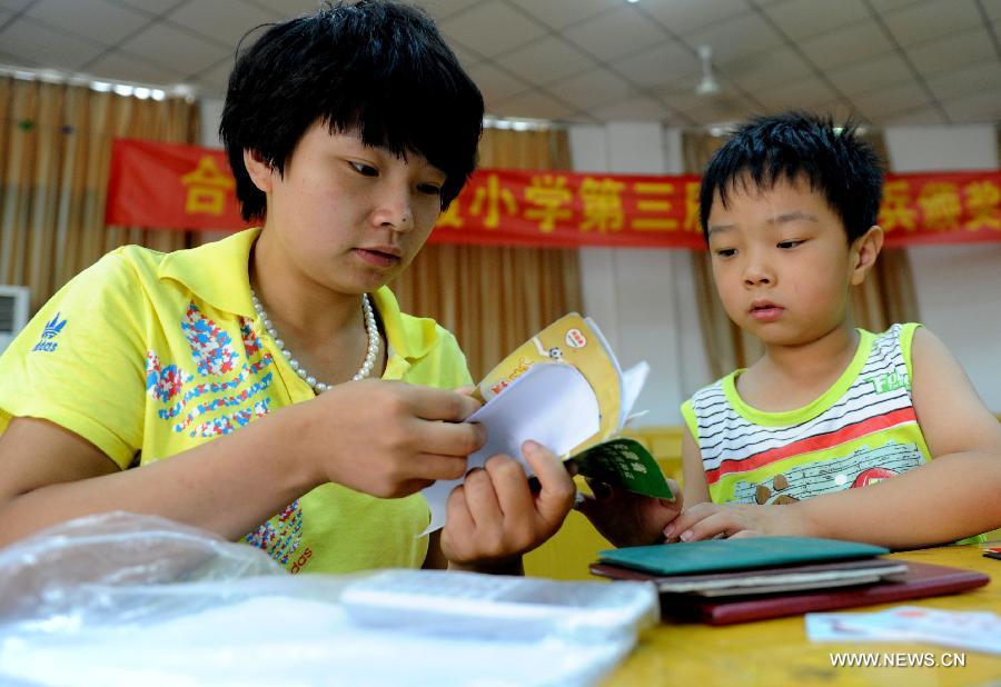 A migrant worker and her child prepare the material for the registration at the Zhaoxia Primary School in Hefei City, east China's Anhui Province, July 16, 2013. A total of 195 sentinel primary schools are opened to the eligible migrant workers' children in the city. (Xinhua/Liu Junxi)