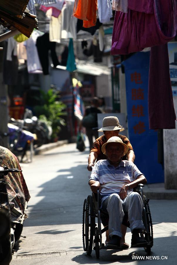 An old woman pushes an old man in a wheelchair in an alley in the Baodai residential area of Yuyuan Street, east China's Shanghai, July 16, 2013. Shanghai suffers from high temperature in recent days. (Xinhua/Pei Xin) 