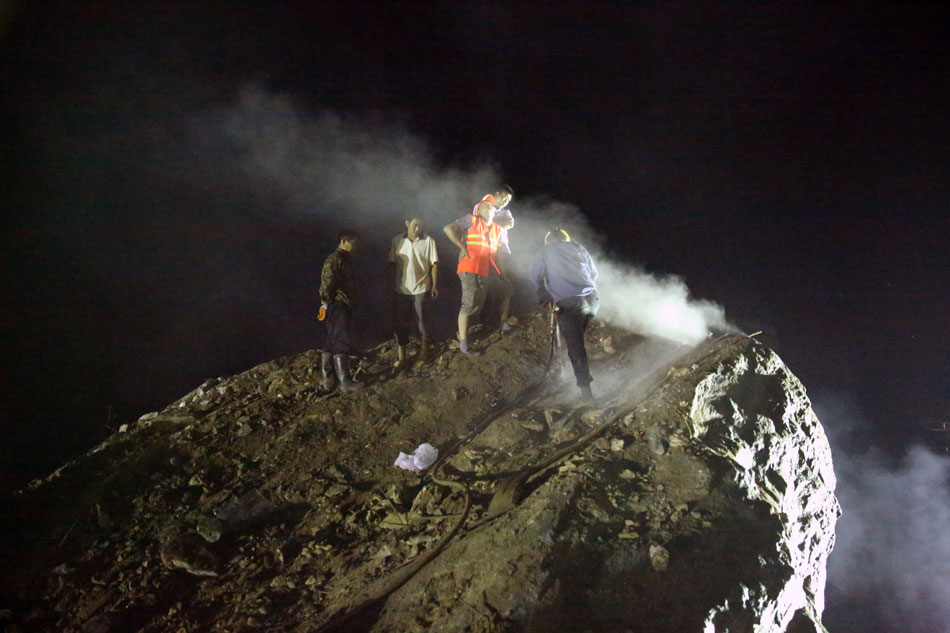 Rescuers try to drill a hole for containing explosives on a huge rock which rolled down with a massive landslide and blocked the traffic of a national road in northwest China’s Shannxi province. (Photo/Xinhua)