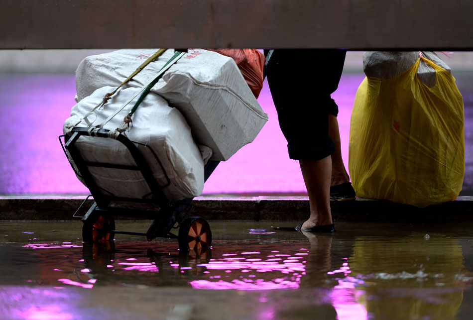 A Shenyang citizen stands in the rain at a bus stop, July 9, 2013. Continuous rainstorm battered the city and caused inconvenience for people’s daily life. (Xinhua/Li Gang)