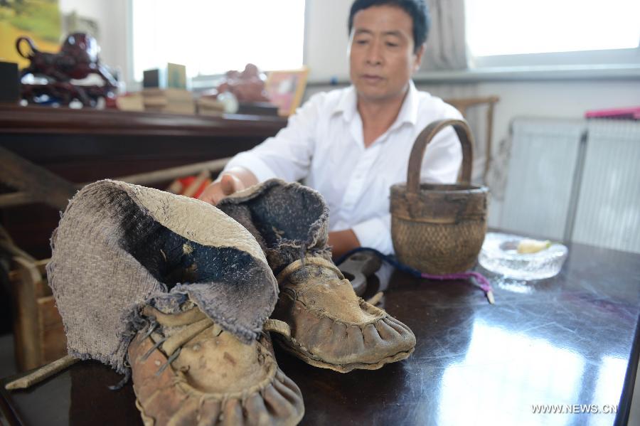 A man demonstrates a pair of piura shoes he just collected in Yanzhangzi Village of the Man Autonomous County of Kuancheng, north China's Hebei Province, July 16, 2013. A museum collecting old stuff was set up in the village to remind the local residents of hard time in the old days. (Xinhua/Wang Min) 