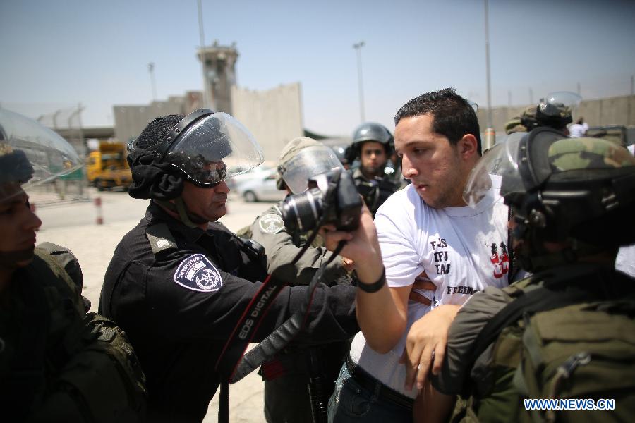 A Palestinian journalist clashes with Israeli soldiers, while Israeli soldiers attacked dozens of Palestinian journalists as they attempted to cross to Jerusalem from Qalandiya checkpoint on July 17, 2013. Palestinian journalists launched a campaign of their freedom of Movement as they are banned from covering with Special Movement Permission from Israel. (Xinhua/Fadi Arouri)