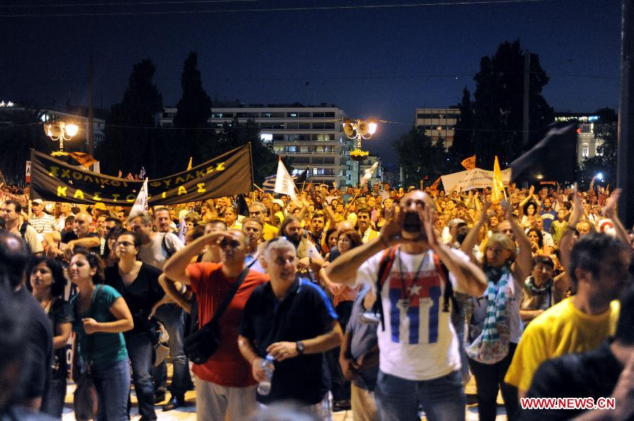 Protesters chant anti-austerity slogans under a banner reading "School guards from the northern city of Kastoria," outside the Greek parliament in Athens on Wednesday, July 17, 2013. Greek parliament approved early on Thursday a new austerity and reform bill which contains mass job cuts in the public sector in a key step to unlock further international bailout aid to the debt-laden country. (Xinhua)