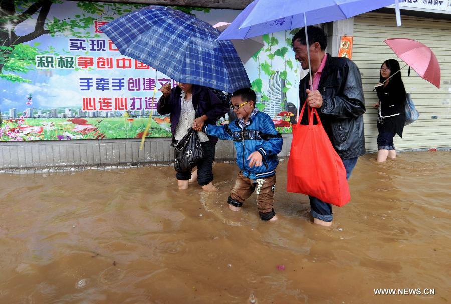 People walk in the flood water in Kunming, capital of southwest China's Yunnan Province, July 19, 2013. Kunming was hit by a heavy rainstorm from Thursday to Friday. (Xinhua/Lin Yiguang)
