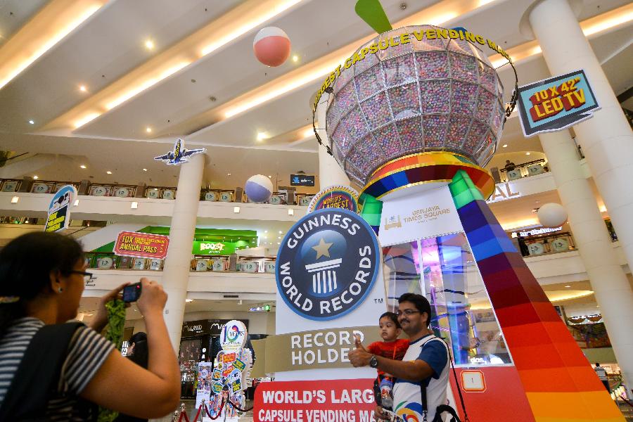 Visitors pose for photos by a capsule vending machine which sets a Guinness World Record for the world's largest one, at a shopping mall in Kuala Lumpur, capital of Malaysia, on July 20, 2013. The machine which can contain 125,000 capsules will be used here for four months. (Xinhua/Chong Voon Chung) 
