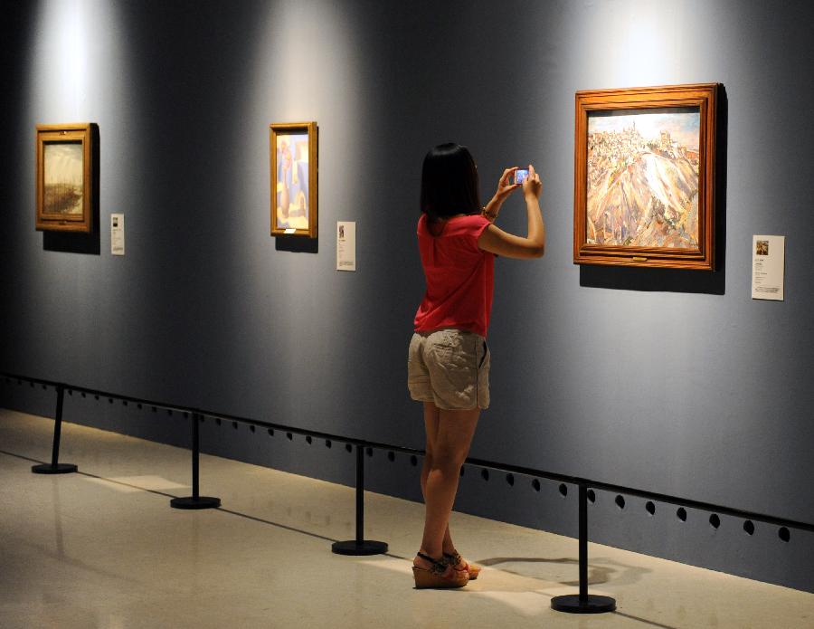 A woman takes pictures of a painting with her cellphone at an exhibition displaying works of art from public collection in northwest England in Zhengzhou, capital of central China's Henan Province, July 21, 2013. Many local citizens spent their weekends by visiting the exhibition, which lasts from June 25, 2013 to Aug. 9, 2013 at Henan Museum. (Xinhua/Li Bo)