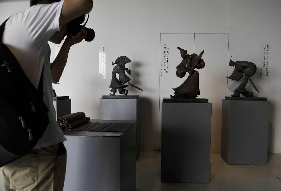 A man takes pictures of sculptures displayed at an exhibition of the awarded sculpture works of 2013 college graduates in Beijing, capital of China, July 21, 2013. These awarded works are presented to the public from July 21, 2013 to July 25, 2013 here. (Xinhua/Lu Peng)
