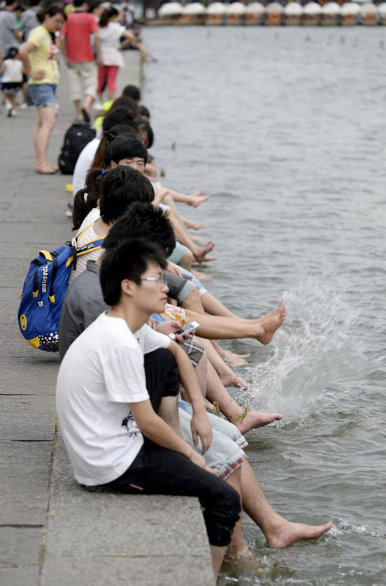 Tourists in Hangzhou, Zhejiang province take off their shoes and dip their feet into the West Lake to cool off. (Chinanews.com)