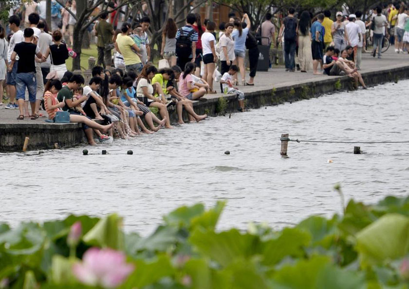 Tourists in Hangzhou, Zhejiang province take off their shoes and dip their feet into the West Lake to cool off. (Chinanews.com)