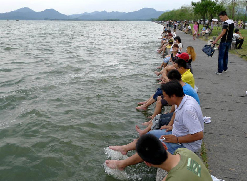 Tourists in Hangzhou, Zhejiang province take off their shoes and dip their feet into the West Lake to cool off. (Chinanews.com)