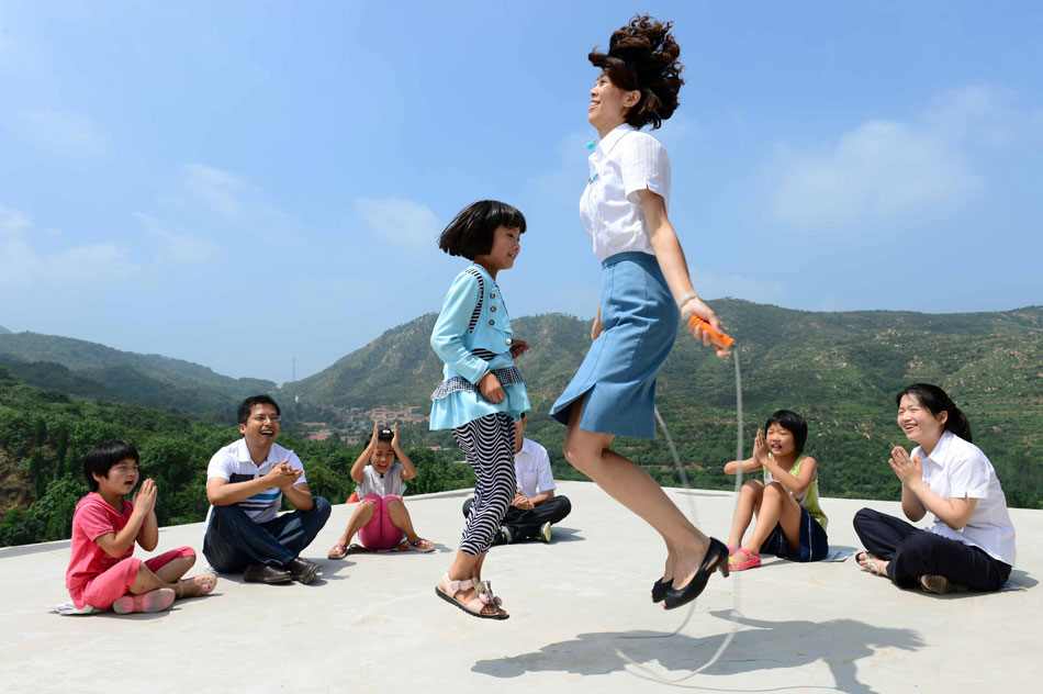 Volunteer from Jinan Changqing Branch State Grid plays jump rope with a left-behind child in Fangzhuang village in Jinan, capital of east China's Shangdong province on July 16, 2013. Volunteers form Jinan Changqing Branch State Grid paid visit to the left-behind children in Fangzhuang village and spent a happy day with them. (Xinhua/Guo Xulei)