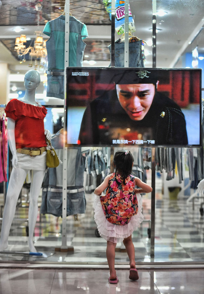 A girl watches TV through a shop window, in Chengbu Miao Autonomous County in central China's Hunan province, July 12, 2013. (Photo/Cheng Tingting)