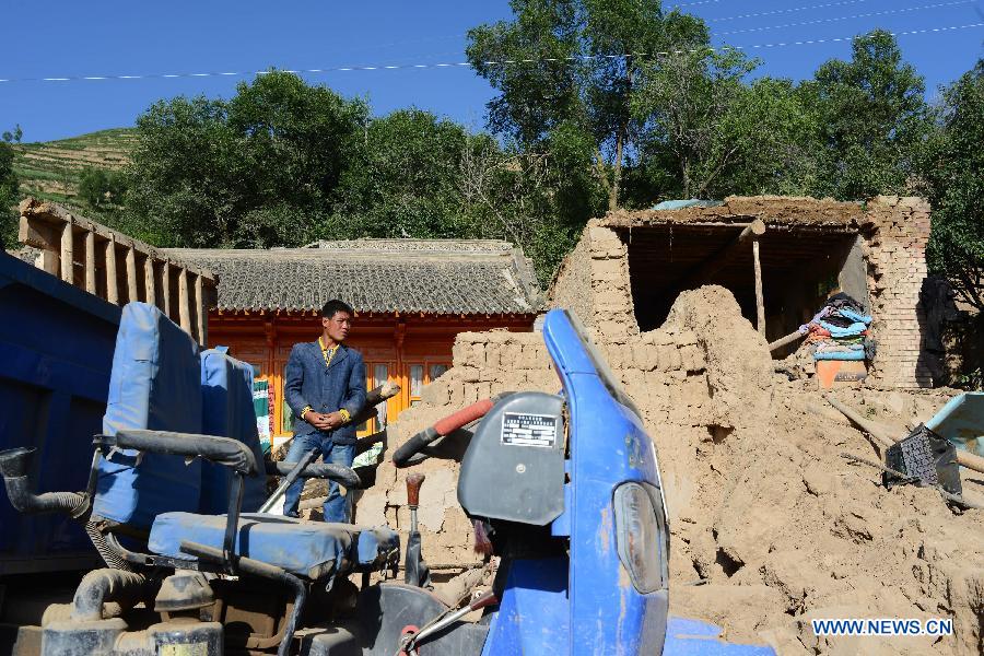 Villager Zhu Chongwei stands on a collapsed wall in front of his house after a quake in Majiagou Village, Meichuan Town, Minxian County, northwest China's Gansu Province, July 22, 2013. A 6.6-magnitude quake jolted the border of Minxian and Zhangxian counties in Gansu at 7:45 a.m. on Monday. (Xinhua/Jin Liangkuai)