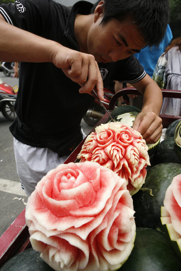 Zhang Yunxiao, a 30-year-old fruit dealer, tries to sell artistic watermelons to a customer in Xiangyang, Hubei province, on Monday, July 23, 2013. Zhang carves vivid flowers like peonies and roses as well as other patterns on the melons. The price for each melon is 20 yuan ($3.26) to 50 yuan. (Photo / China Daily)