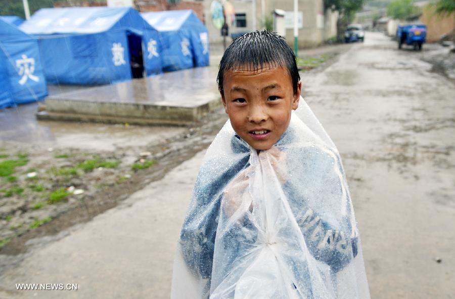 A boy plays in rain at a temporary settlement for quake-affected people in Qingtu Village of Minxian County, northwest China's Gansu Province, July 24, 2013. A rainfall hit the quake-jolted region in Gansu on Wednesday. The death toll has climbed to 95 in the 6.6-magnitude earthquake which jolted a juncture region of Minxian County and Zhangxian County in Dingxi City Monday morning. (Xinhua/Liu Xiao)