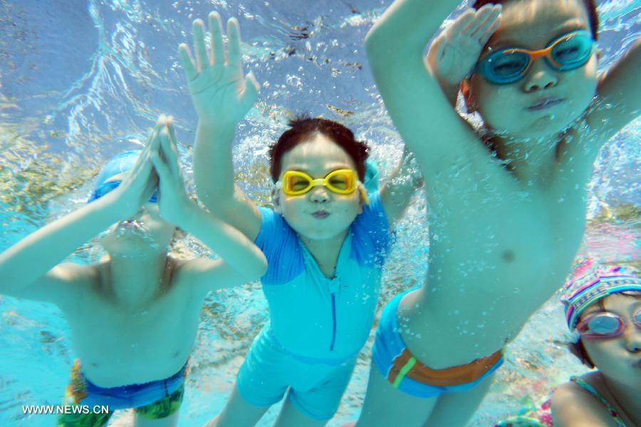 Photo taken under water on July 24, 2013 shows children swimming in an outdoor swimming pool of a park in Hangzhou, capital of east China's Zhejiang Province. Local meteorological observatory issued a red alert for high temperature, warning that the highest temperature will reach 40.4 degrees Celsius on Wednesday, which also marked the hottest day on record. (Xinhua/Li Zhong) 