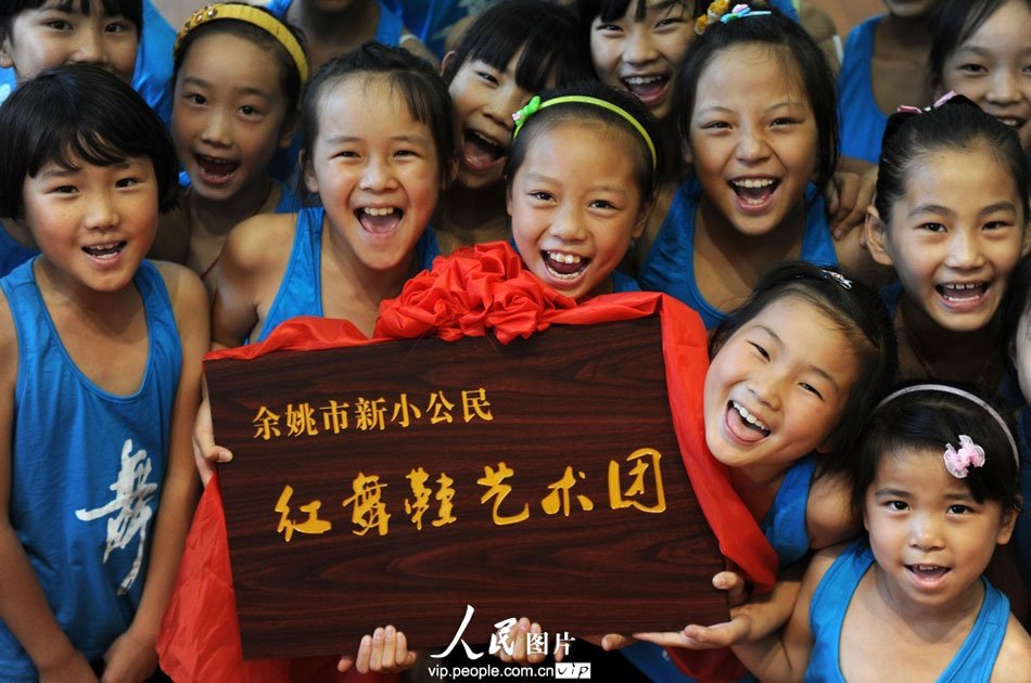Children of migrant workers grin when they see the new plaque of their dance troupe in Yuyao City, east China’s Zhejiang province. (Photo by Chen Binrong/ vip.people.com.cn)
