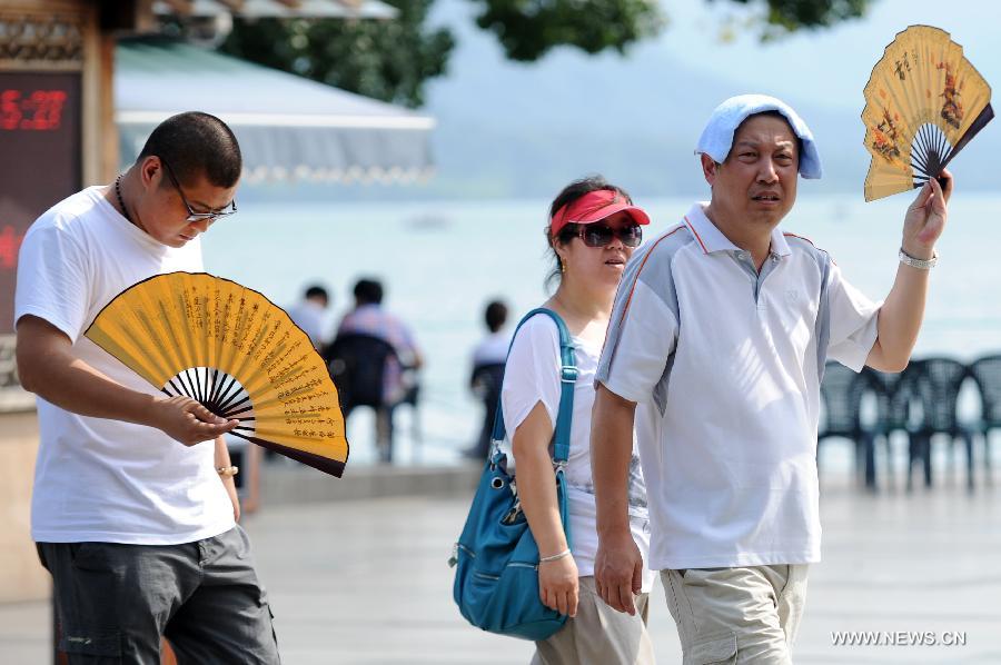 A tourist (R) holds a fan for shelter beside the West Lake in Hangzhou, capital of east China's Zhejiang Province, July 25, 2013. The highest temperature in Hangzhou reached 40.3 degrees Celsius on Thursday. (Xinhua/Ju Huanzong)
