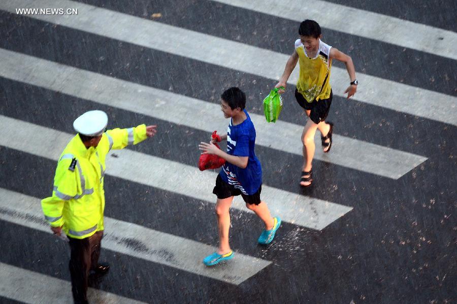 A traffic policeman directs children to cross the road in torrential rain in Jinan, capital of east China's Shandong Province, July 29, 2013. A sudden downpour hit the city on Monday afternoon. (Xinhua/Guo Xulei)