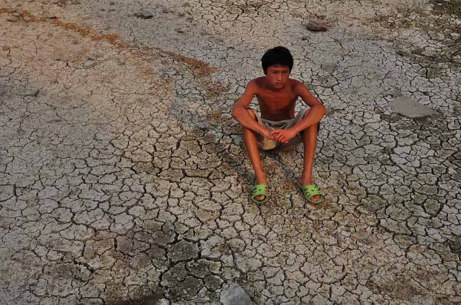 A boy sits on the chapped riverbeds near the Wantou Bridge over Yaojiang River in Ningbo, east China's Zhejiang Province, July 28, 2013. Unrelenting heat in Ningbo has drawn the water table of the Yaojiang River down and parts of the beds were chapped, which led to the death of mussels and fish. (Xinhua/Hu Xuejun)