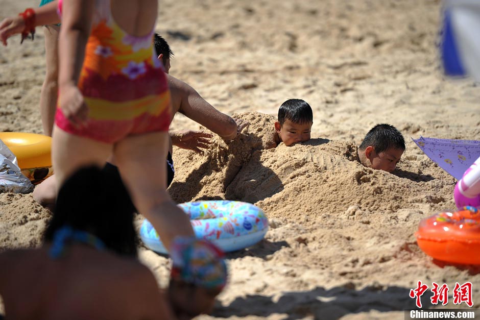 Children bury themselves in the sands to cool off. Heat wave tightens grip on most China’s cities on July 28; Beijing issued second orange alert of heat. (Photo/CNS) 