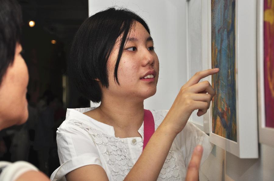 Zhang Yuqing (R), a young artist, introduces her works to visitors at the exhibition "The Strength of Natural Impulses" in Beijing, capital of China, July 30, 2013. Jointly contributed by French artist Francois Bossiere and four Chinese artists Zhang Sen, Zhang Yuqing, Sun Qianwei and Xie Hong, the exhibition concerned with visual art will be held from July 30 to Aug. 6 in Beijing. (Xinhua/Wang Jingqiang) 